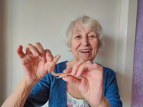 Cheerful older woman smiling and holding her new denture