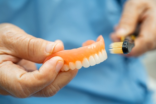 Older hands cleaning an upper full denture with a brush