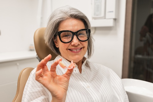 Smiling older woman in a dental chair holding up her partial denture