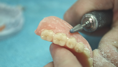 Denturist shaping and polishing the teeth of a denture in the lab